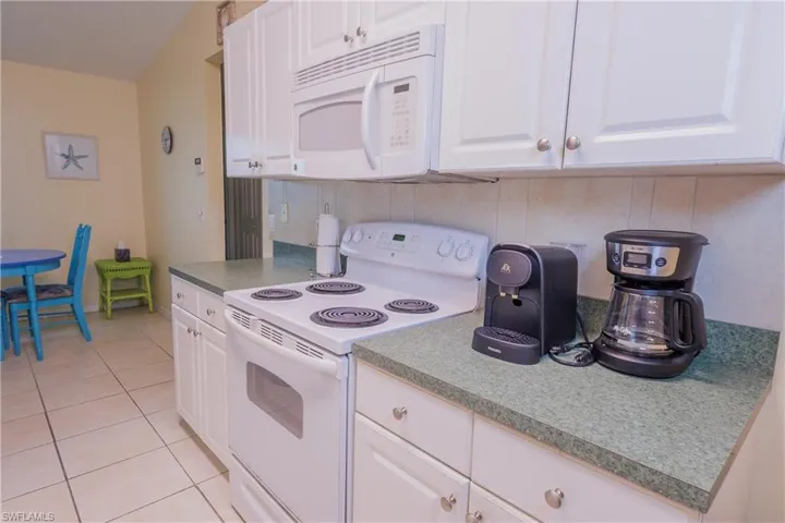 Kitchen featuring white appliances, light tile patterned floors, white cabinetry, and tasteful backsplash