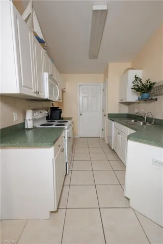 Kitchen featuring white appliances, decorative backsplash, white cabinets, dark countertops, and light tile patterned flooring