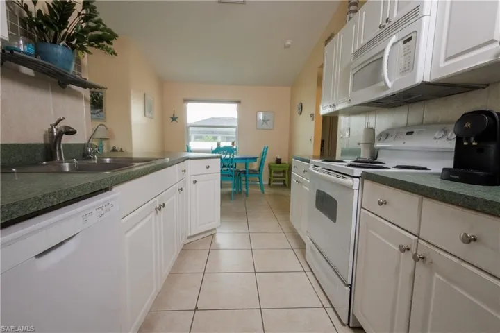 Kitchen featuring white appliances, dark countertops, vaulted ceiling, backsplash, and light tile patterned floors