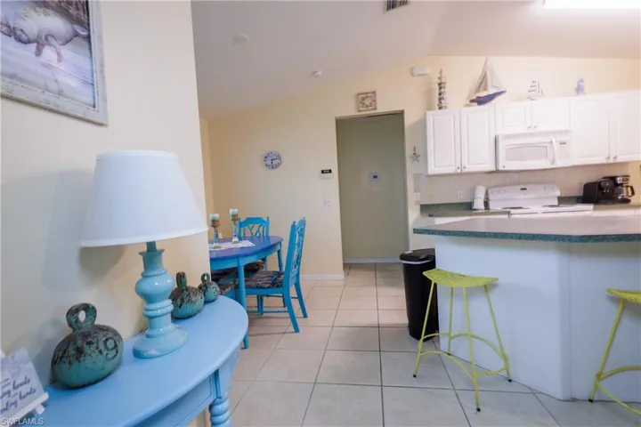 Kitchen featuring lofted ceiling, white appliances, white cabinets, a breakfast bar, and dark countertops