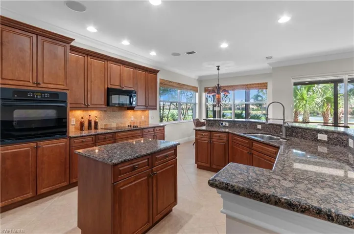 Kitchen featuring an island with sink, hanging light fixtures, sink, black appliances, and crown molding