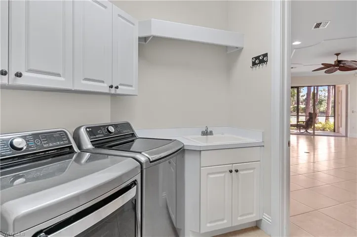 Clothes washing area with cabinets, ceiling fan, light tile patterned flooring, washing machine and dryer, and sink