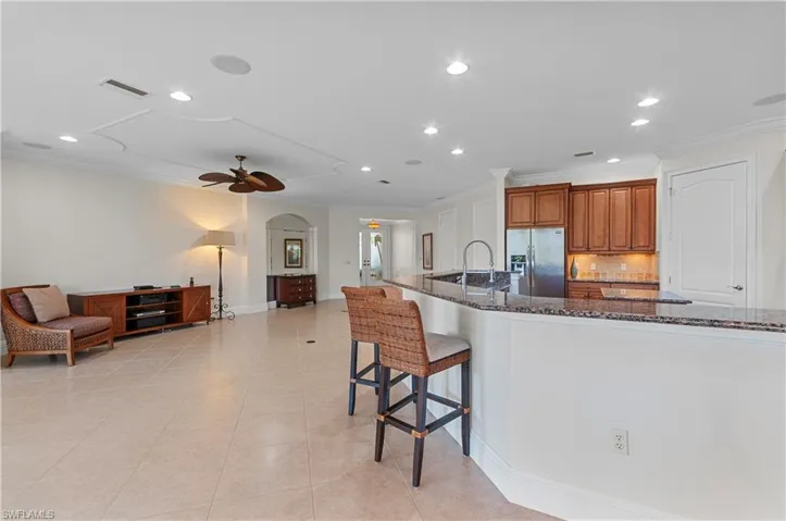 Kitchen with ceiling fan, backsplash, a breakfast bar, stainless steel fridge with ice dispenser, and dark stone counters