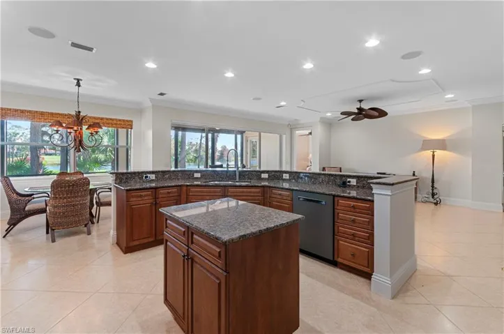 Kitchen featuring an island with sink, dark stone counters, dishwasher, pendant lighting, and sink