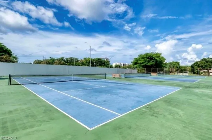 Multiple outdoor tennis courts featuring blue playing surfaces and green surrounds