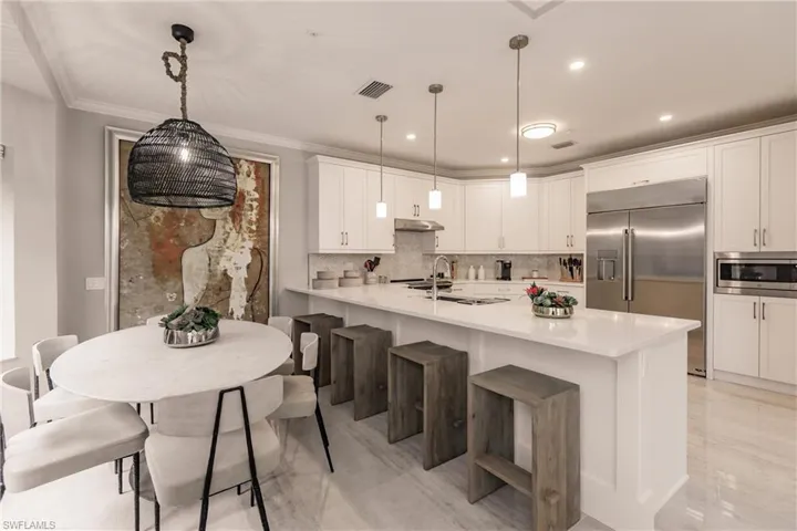 Kitchen with built in appliances, tasteful backsplash, a breakfast bar, hanging light fixtures, and white cabinetry