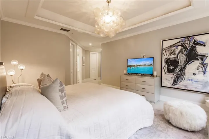 Carpeted bedroom with crown molding, a raised ceiling, and an inviting chandelier
