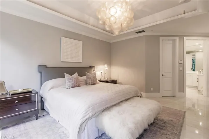 Bedroom featuring a raised ceiling, an inviting chandelier, ensuite bathroom, and crown molding