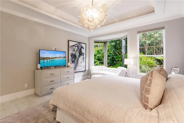 Bedroom featuring an inviting chandelier, a raised ceiling, light carpet, and ornamental molding