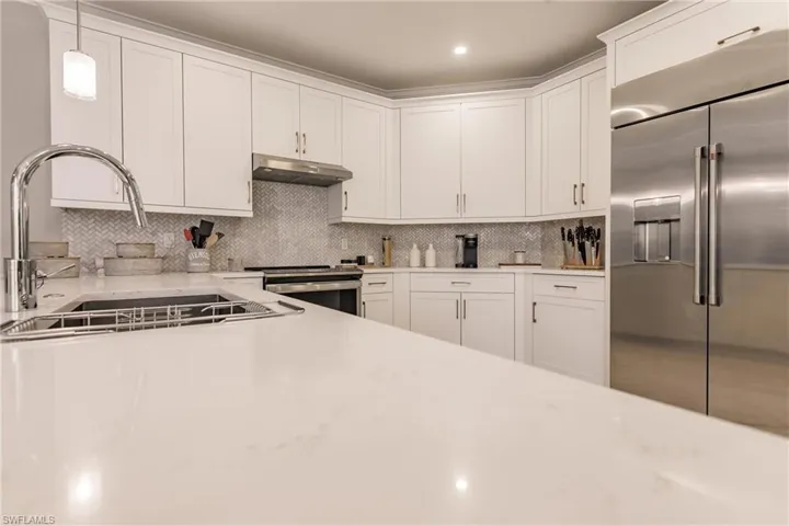 Kitchen with white cabinetry, backsplash, stainless steel appliances, sink, and hanging light fixtures