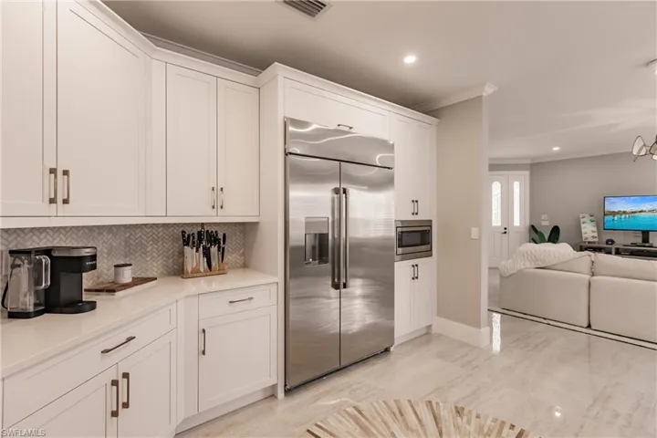 Kitchen featuring white cabinetry, crown molding, built in appliances, and tasteful backsplash