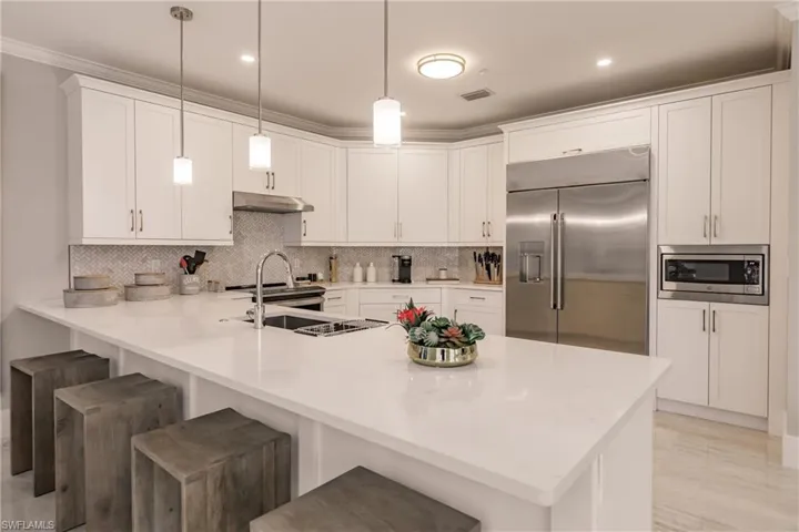 Kitchen with built in appliances, pendant lighting, a kitchen bar, kitchen peninsula, and white cabinetry