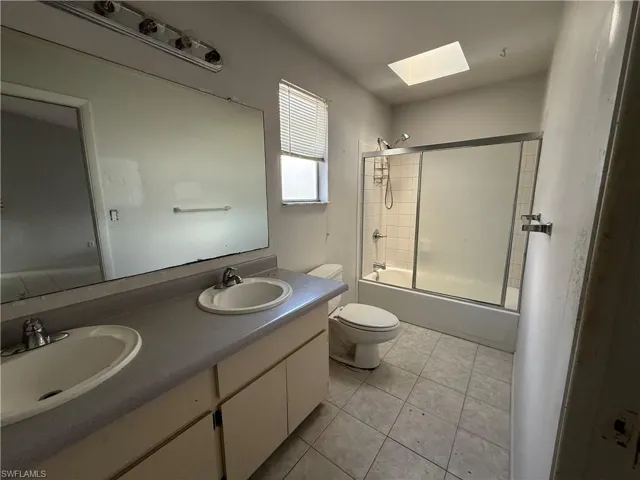 Bathroom with double vanity, a skylight, bath / shower combo with glass door, and light tile patterned floors