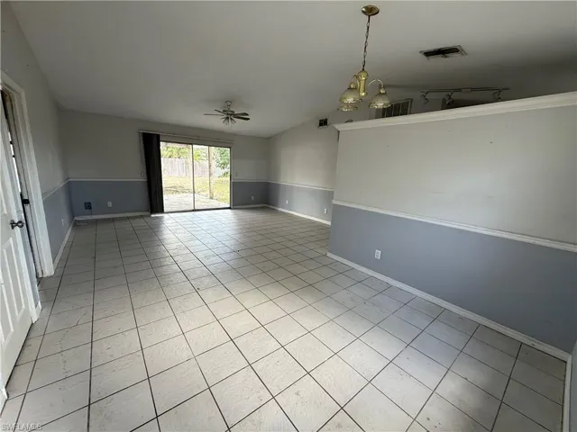 Spare room featuring lofted ceiling, light tile patterned floors, suspended lighting, and a ceiling fan