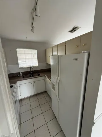 Kitchen featuring fridge, track lighting, tasteful backsplash, light tile patterned floors, and dark countertops