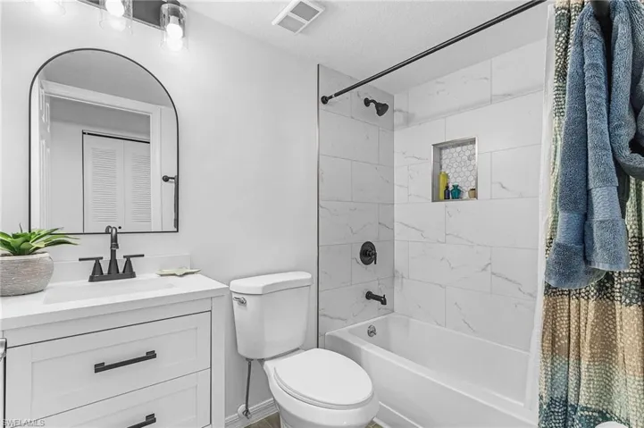 Bathroom featuring visible vents, vanity, toilet, a textured ceiling, and shower / washtub combination