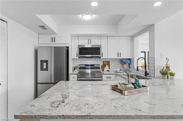 Kitchen with white cabinets, light stone counters, a sink, appliances with stainless steel finishes, and backsplash