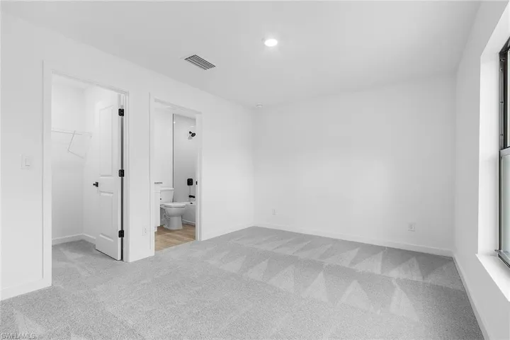 Unfurnished bedroom with carpet floors, a walk in closet, connected bathroom, and recessed lighting