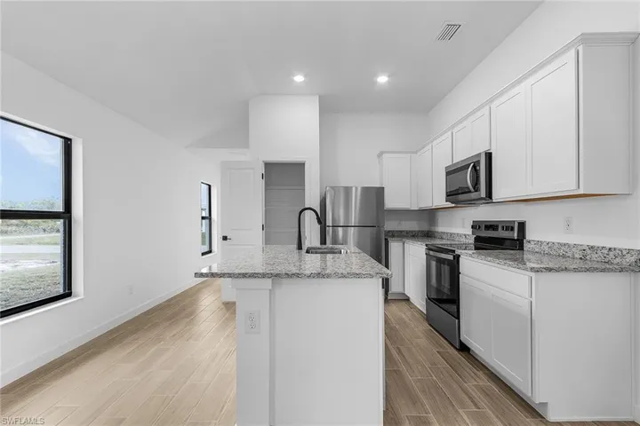 Kitchen featuring stainless steel appliances, a center island with sink, light stone countertops, white cabinetry, and recessed lighting