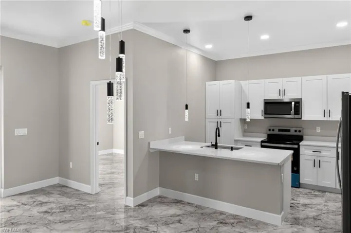 Kitchen featuring stainless steel appliances, white cabinetry, ornamental molding, hanging light fixtures, and a peninsula
