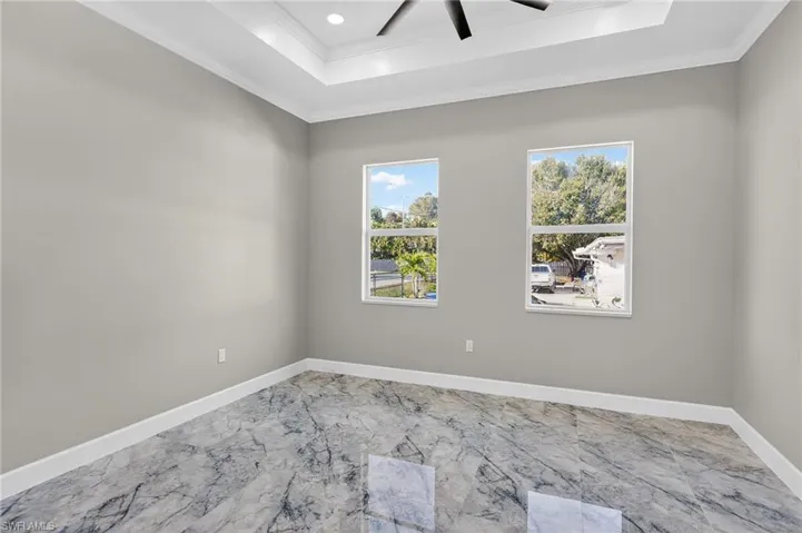 Unfurnished room with a tray ceiling, ornamental molding, marble finish flooring, and a ceiling fan