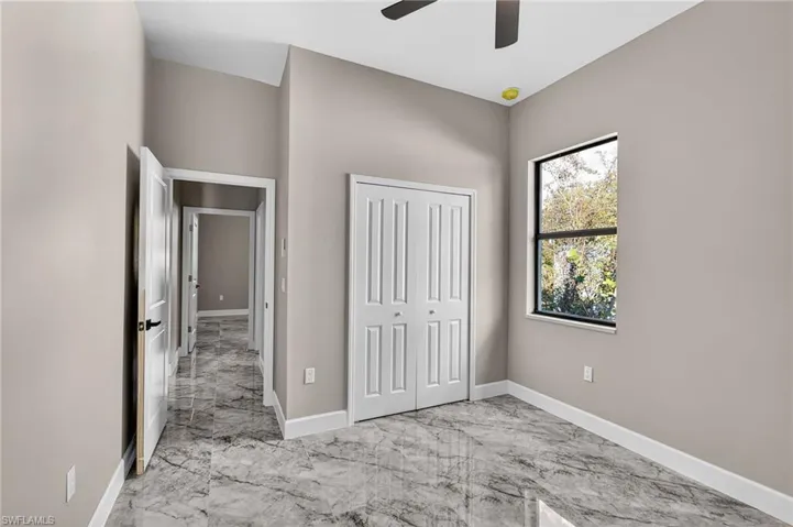Unfurnished bedroom featuring light marble finish flooring, a closet, and a ceiling fan