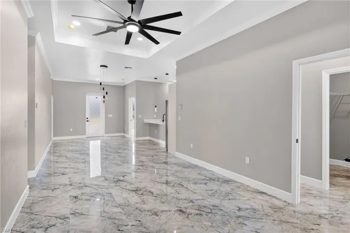 Unfurnished living room with a tray ceiling, light marble finish flooring, ceiling fan, crown molding, and recessed lighting