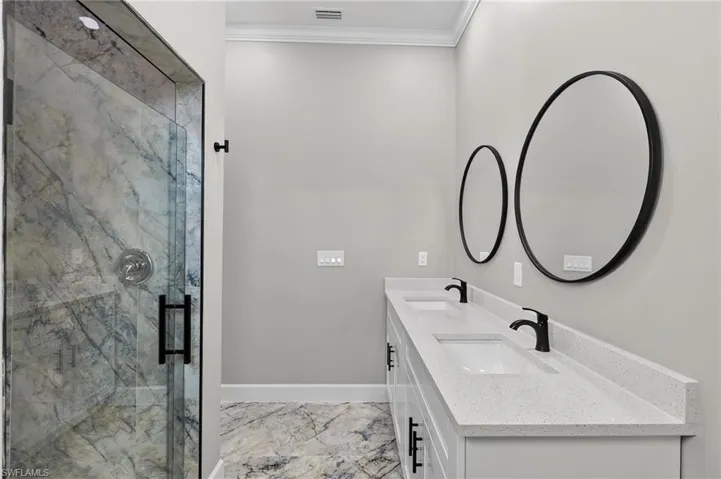 Full bathroom featuring light marble finish flooring, ornamental molding, double vanity, and a marble finish shower
