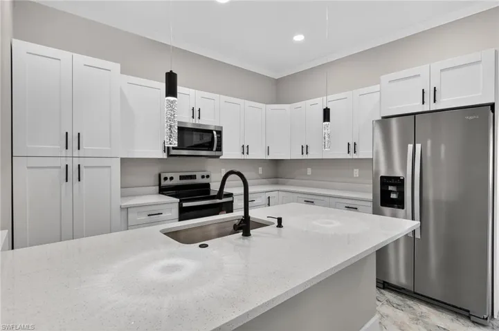 Kitchen featuring appliances with stainless steel finishes, hanging light fixtures, light stone counters, ornamental molding, and white cabinets