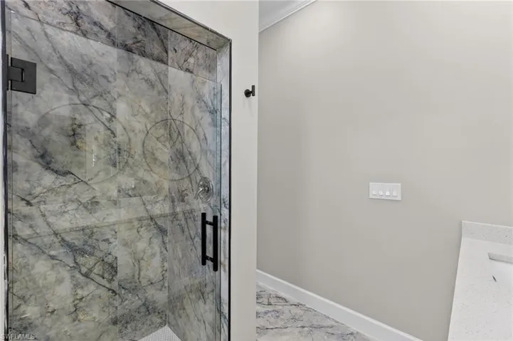 Bathroom featuring vanity, light marble finish flooring, and a marble finish shower