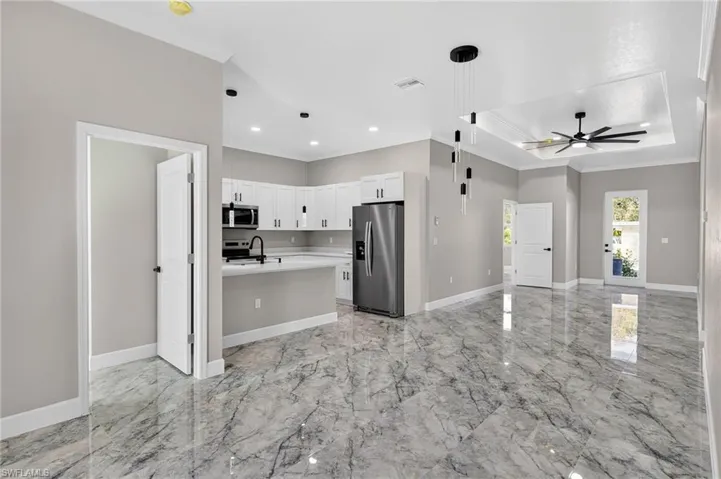 Kitchen featuring open floor plan, ornamental molding, pendant lighting, appliances with stainless steel finishes, and a raised ceiling