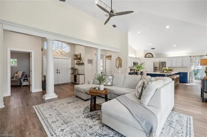 Living room featuring a ceiling fan, light wood-type flooring, high vaulted ceiling, and ornate columns