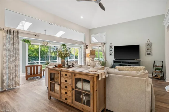Living area with visible vents, baseboards, lofted ceiling with skylight, ceiling fan, and wood finished floors
