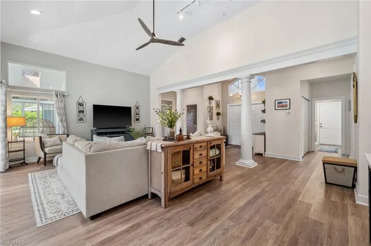 Living room featuring decorative columns, high vaulted ceiling, light wood-style flooring, and a ceiling fan