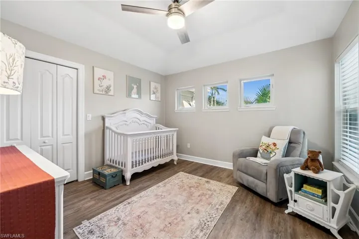 Bedroom with wood finished floors, a ceiling fan, baseboards, a closet, and a nursery area