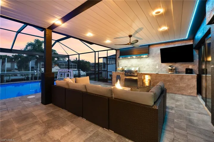 Patio terrace at dusk with an outdoor living space, grilling area, screened enclosure, ceiling fan, and an outdoor kitchen