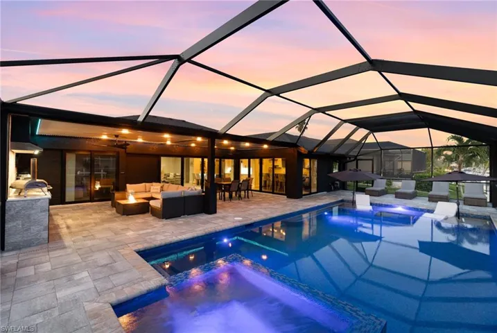 Pool at dusk with an outdoor living space, a lanai, and 360 degree hot tub, and outdoor kitchen
