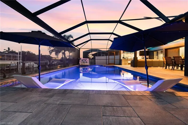 Pool at dusk with a paver deck and screened enclosure