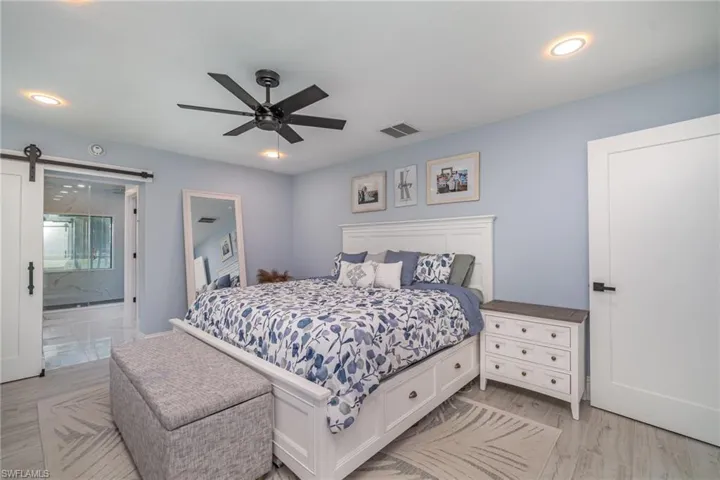 Bedroom with walk in closet, a barn door, tile plank floors, ensuite bathroom, and ceiling fan
