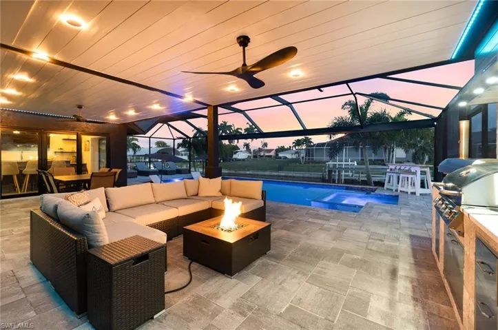 Screened lanai at dusk featuring ceiling fan, outdoor living space, and summer kitchen