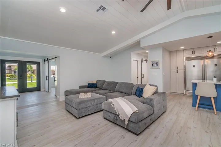 Living room featuring vaulted shiplap ceiling w a barn door, French doors, tile plank floors