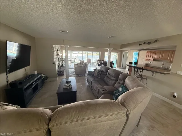 Living room featuring visible vents, a textured ceiling, decorative columns, and baseboards