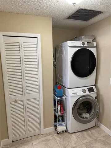 Laundry area featuring light tile patterned flooring, a textured ceiling, and stacked washer / dryer