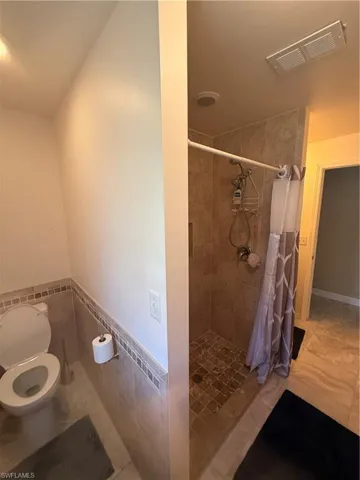Bathroom featuring tile walls, tile patterned floors, toilet, and a shower with shower curtain
