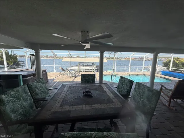 View of patio with a ceiling fan, glass enclosure, a water view, and an outdoor pool