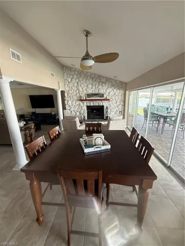 Dining space with decorative columns, visible vents, a ceiling fan, vaulted ceiling, and a stone fireplace
