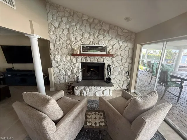 Living area featuring high vaulted ceiling, decorative columns, visible vents, and a stone fireplace