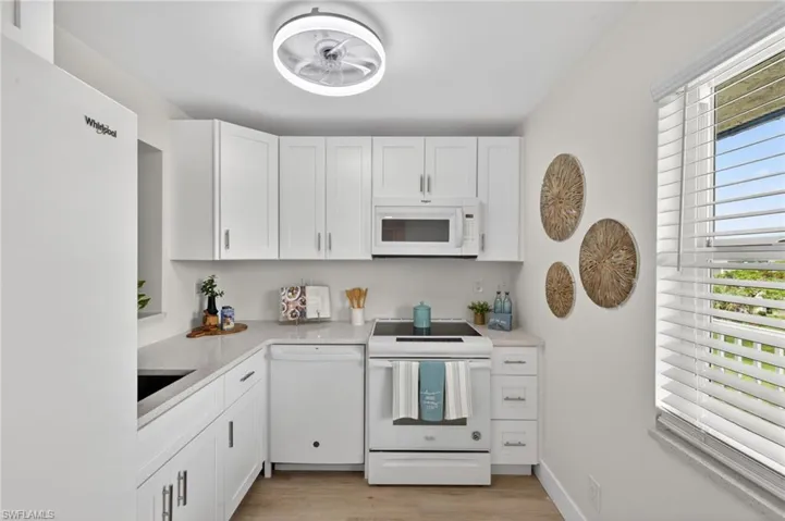 Kitchen with quartz countertops, ceiling fan, white appliances and pass through window
