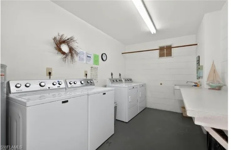 Dedicated laundry room featuring two top-load washing machines, two electric dryers, and a utility sink