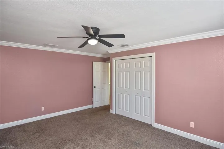 Unfurnished bedroom featuring carpet, ceiling fan, crown molding, and a closet